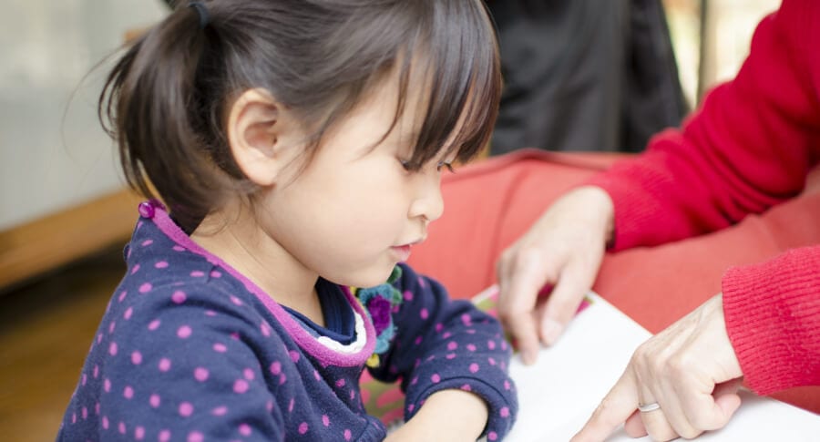 Petite fille fasant de la lecture avec l'aide d'un parent