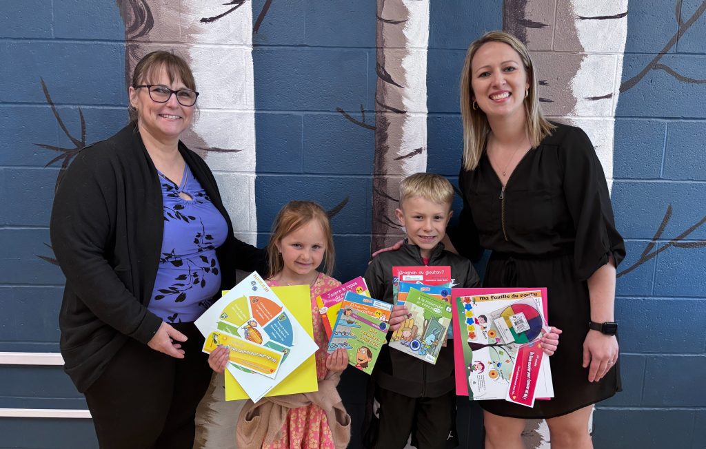 Lancement 2025 du programme Un livre-courrier pour bouquiner cet été ! à l’école Élémentaire Sacré-Cœur de Grand-Sault. De gauche à droite : Carole Caron (bénévole), Lydia Ouellette (maternelle), Jamie Sauvageau (1re année) et Hélène Daigle (enseignante en littératie et directrice adjointe à l’école Élémentaire Sacré-Cœur).